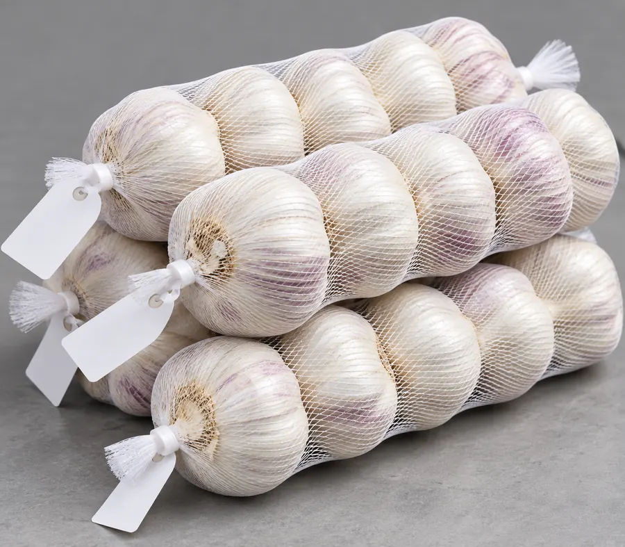 Garlic bulbs in white net sleeves with blank tags (AI-generated image)
